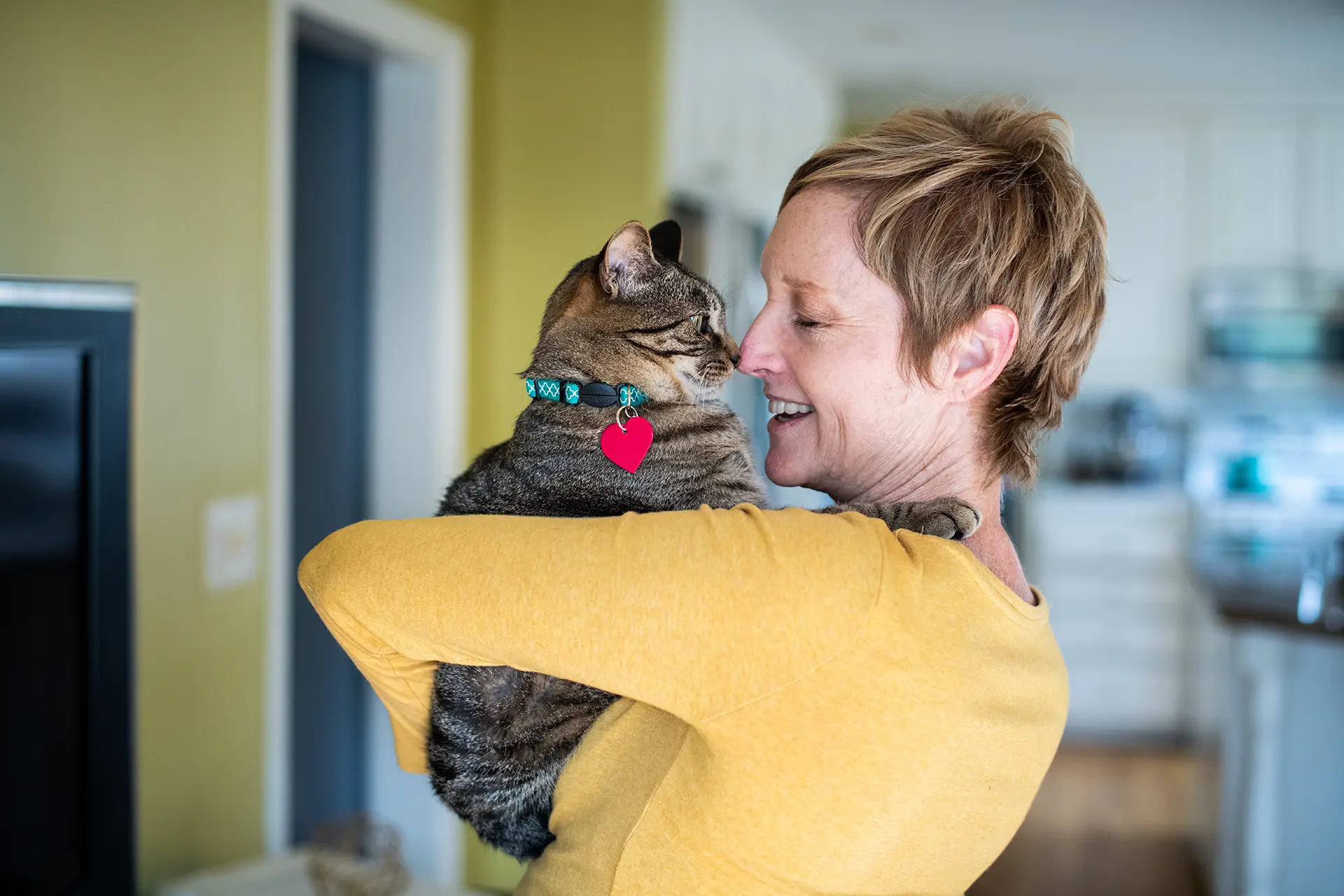 Woman with short blonde hair wearing a yellow sweater is holding a cat